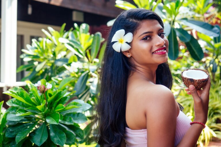 Home-Remedies-for-Hair-Care-One-Health-Assist, indian woman applying coconut oil dark brunette long hair in a hand on green summer park nature tropical